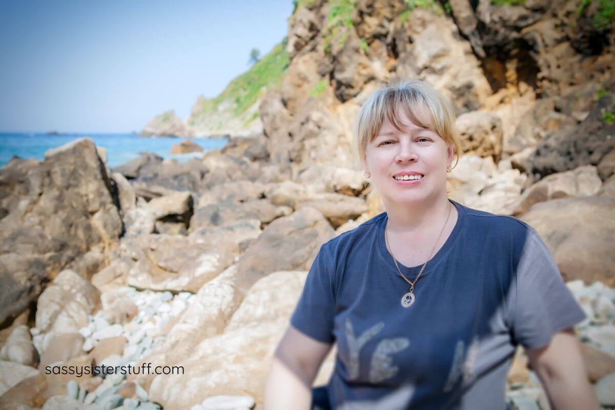 middle aged woman traveler sitting on large rocks on the edge of a body of water.