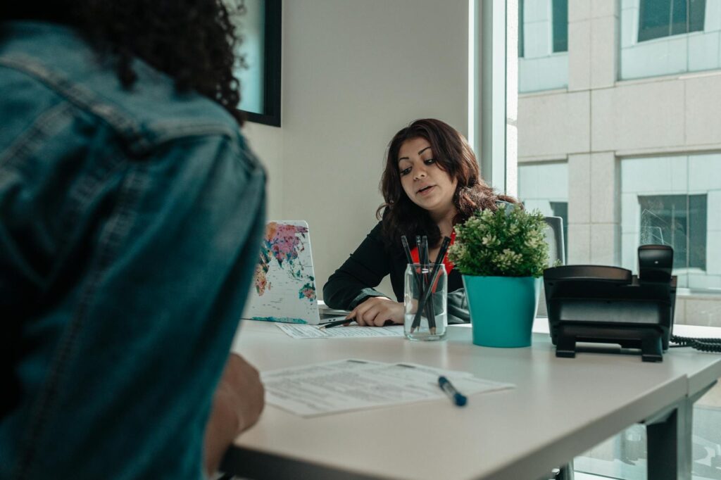 Two individuals in an office engaged in a discussion with paperwork.
