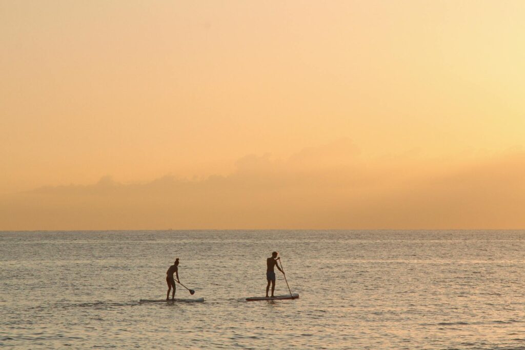 Two people paddleboarding at sunset in the tranquil waters of Barcelona.