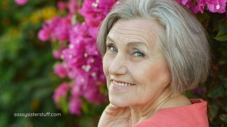 beautiful older woman outside with pink flowers behind her.