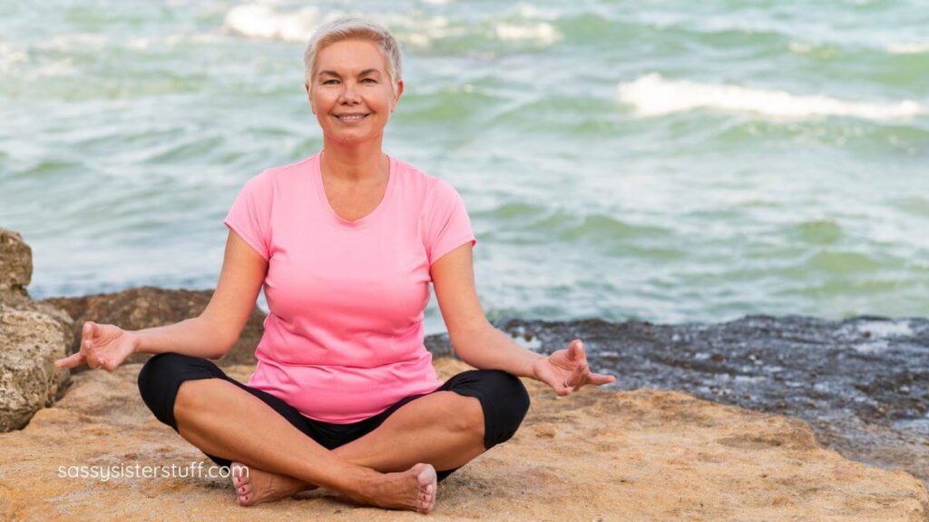 middle aged woman doing yoga next to a body of water to build mental resilience.
