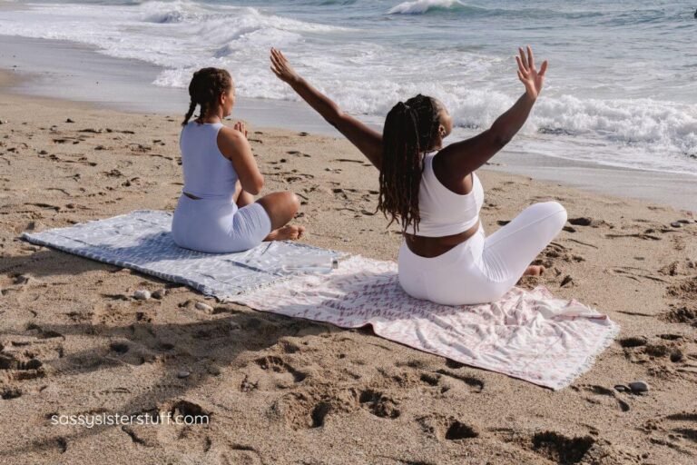 two women practice yoga and meditation on the beach as part of their wellness routines that are actually sustainable.