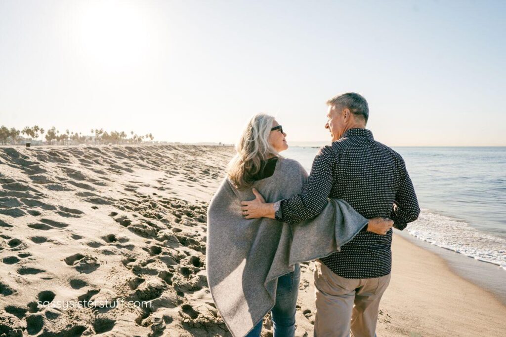 an older couple walks along the beach peacefully as part of their wellness routine.