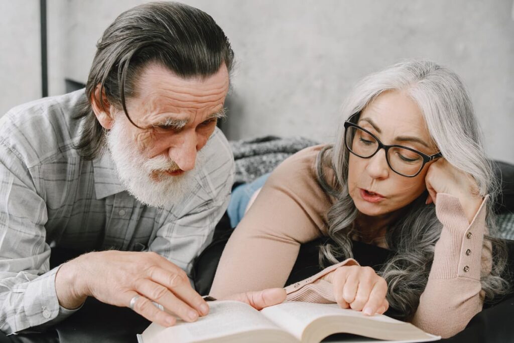 Happy aged married couple relaxing together at home. Senior couple reading book on bed.