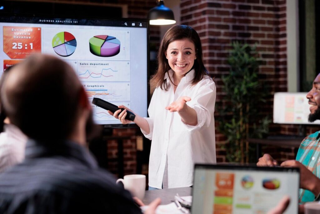 Smiling business employee standing in front of tv screen with sales statistics tal