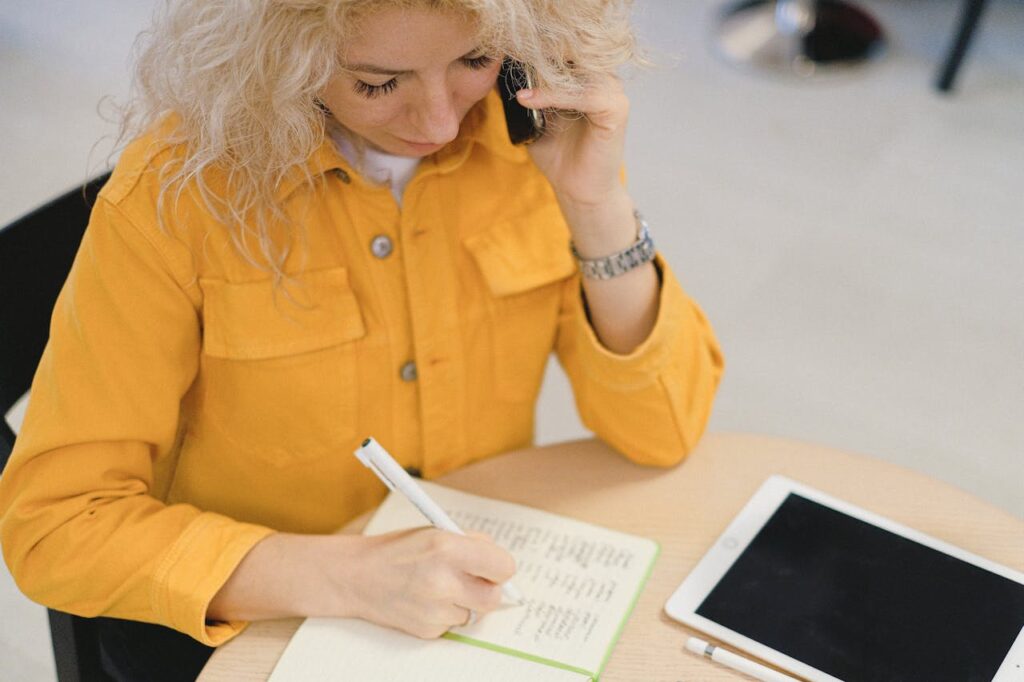 Woman writing in planner during business call