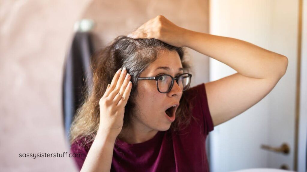 middle aged woman looking in the mirror and is shocked to see gray hair.