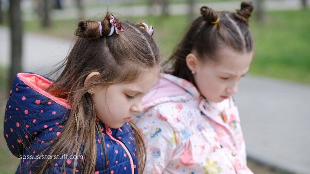 two little girls sit on a bench looking guilty about their behavior.