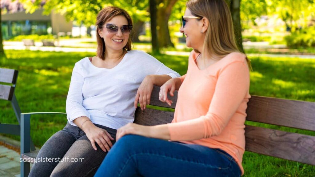 middle aged women sitting on a bench in the part supporting each other.