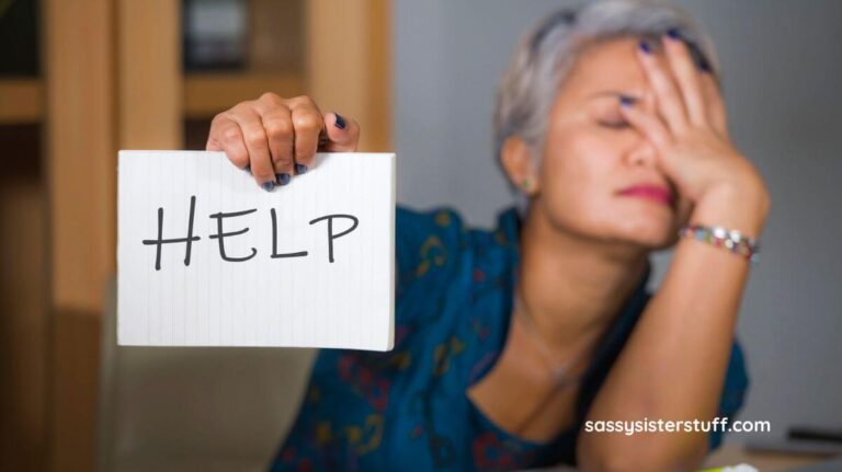 middle aged woman with her hand to her forehead overwhelmed by clutter holding a sign that says HELP.