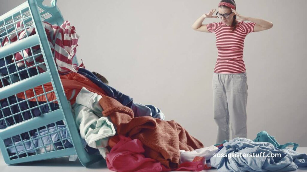 woman standing with her hands on her temples looking overwhelmed by clutter and a huge basket of clothes that overflows in front of her.