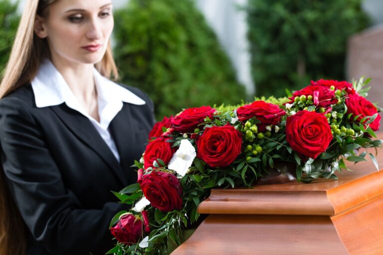 woman standing looking at a casket with red roses on top of it