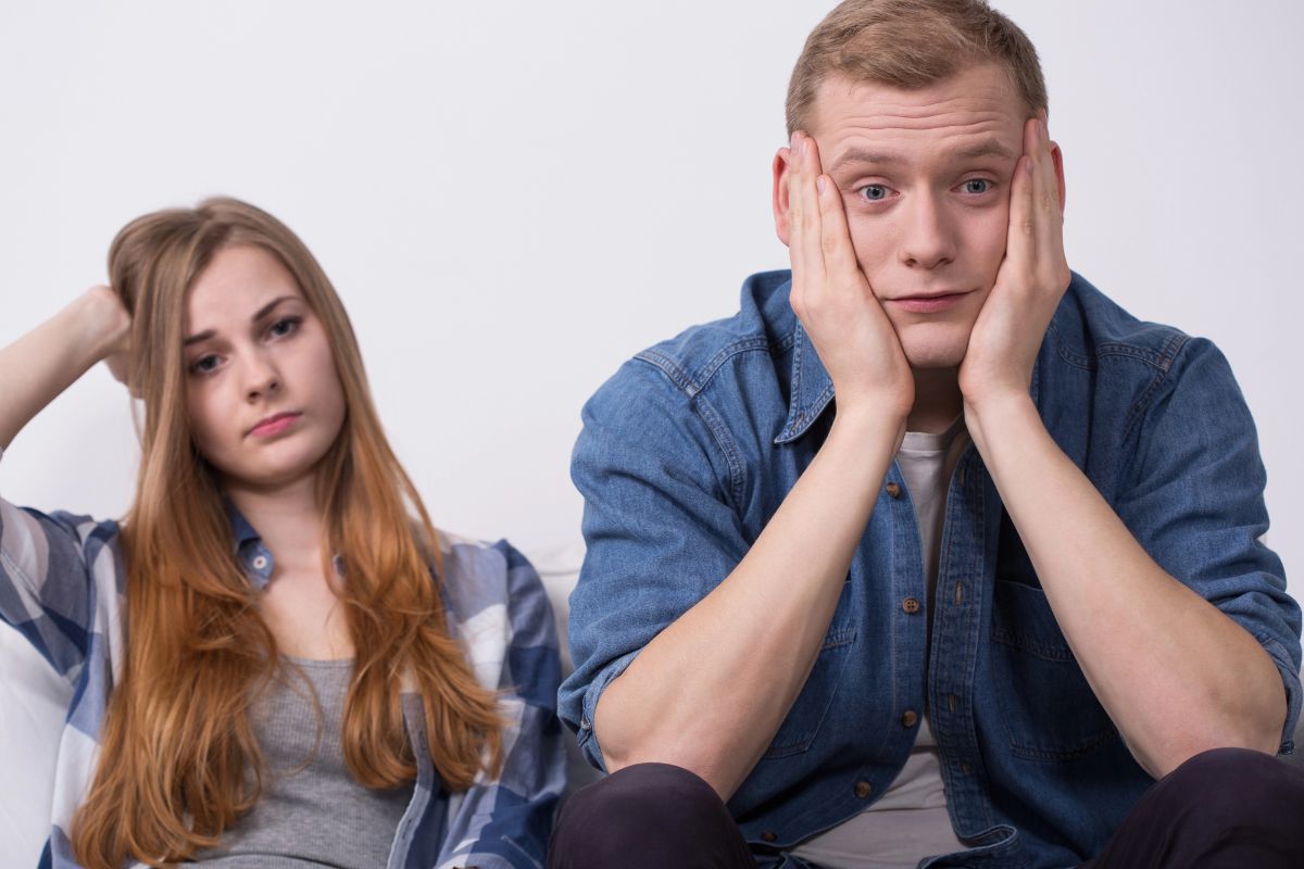young couple sitting, man with hands on his face, woman hand in her hair looking bored.