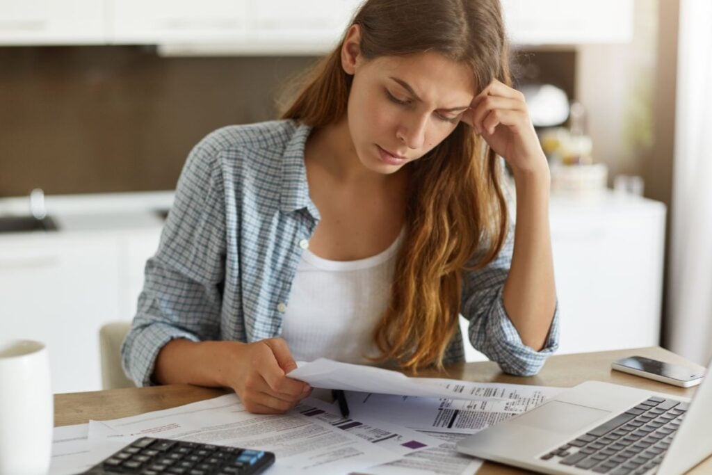 Indoor shot of casually dressed young woman holding papers in her hands, calculating family budget