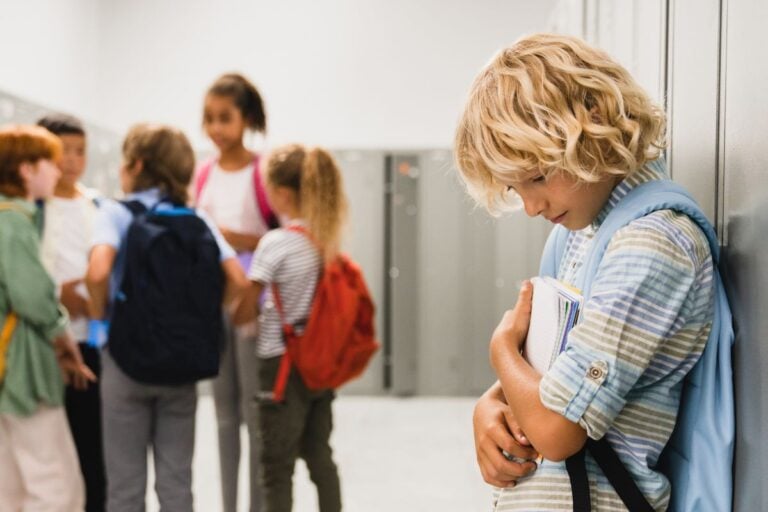 Lonely sad schoolboy crying while all his classmates ignoring him.