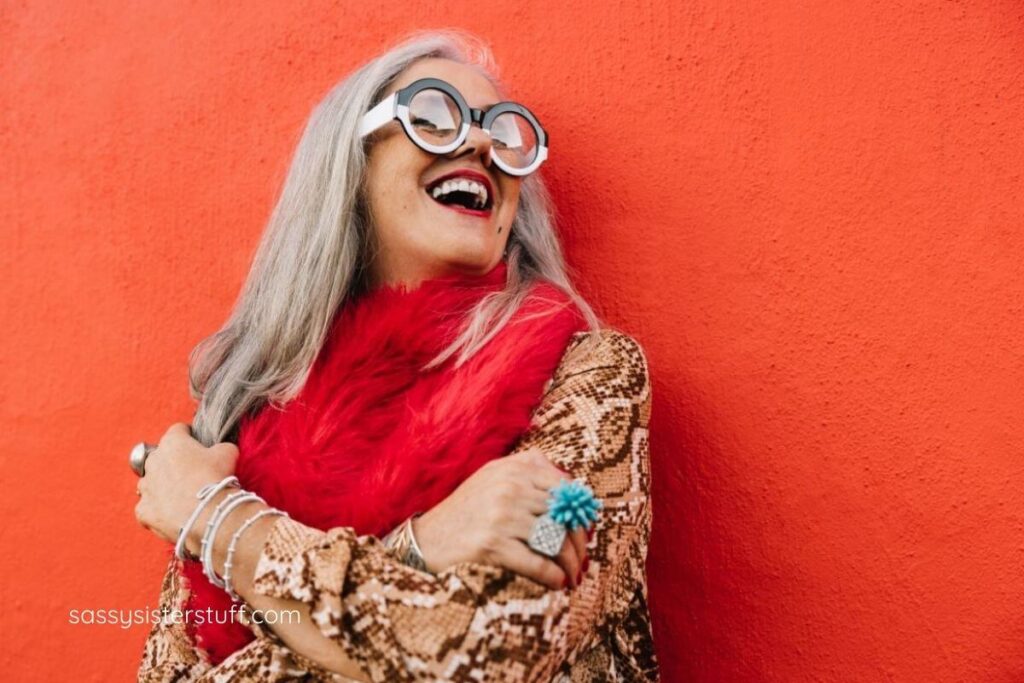 older woman dressed in bright colors and large eye glasses laughing bolding.