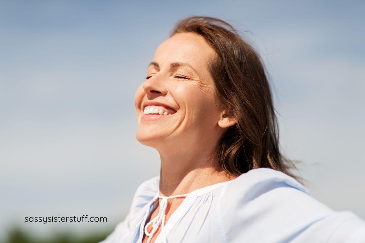 middle aged woman smiling up in the sunshine with her eyes closed thinking about affirmations for overthinking.
