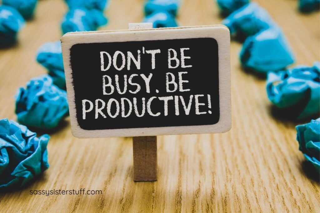 a small sign that says "Don't be busy, be productive" stands on a table with a bunch of scrap paper someone has wasted time rolling them up.