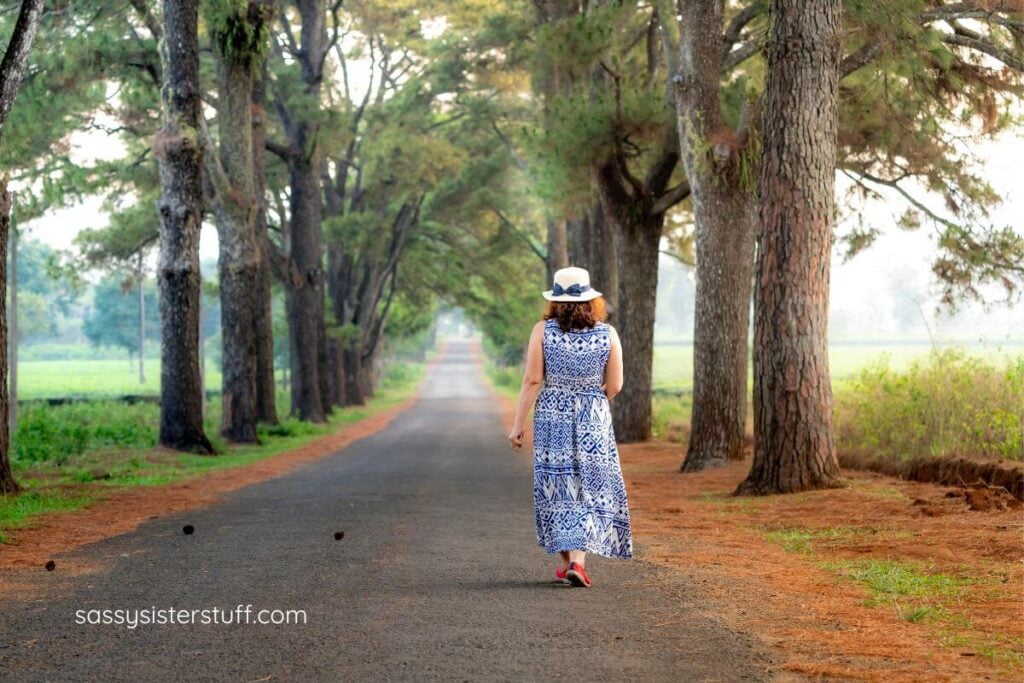 middle aged woman goes for a walk down a long road between trees to contemplate her adult child going no-contact.