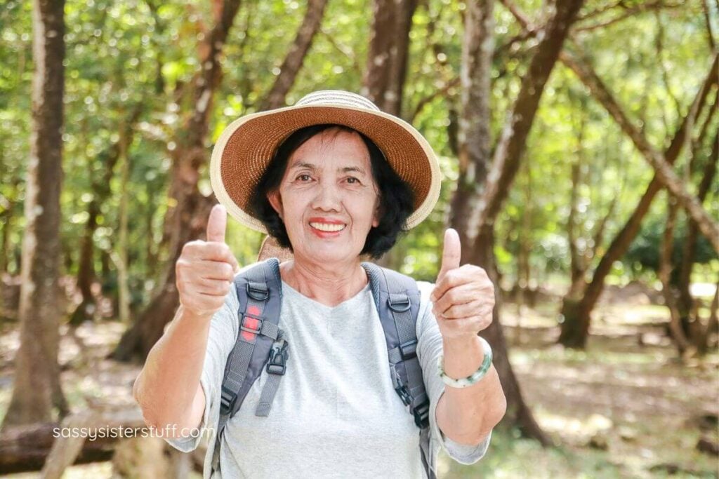 happy middle aged Asian woman hiking gives two thumbs up on her journey.