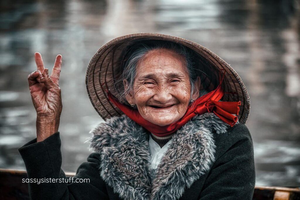 Sernior Indian woman with straw hat on smiles a toothless smile and gives a peace sign.
