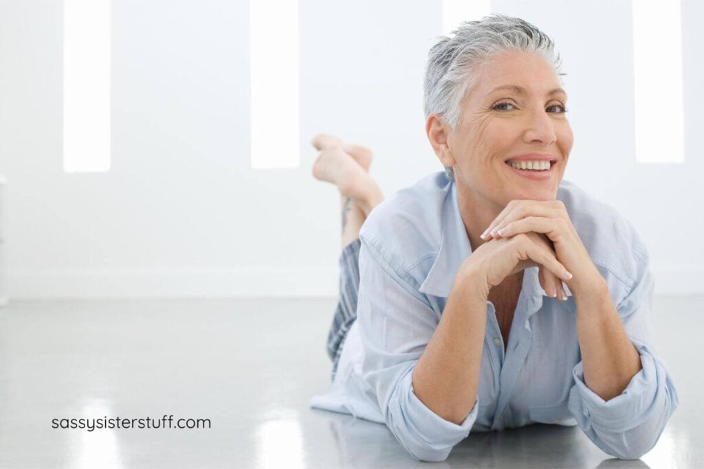 happy woman in midlife laying on her tummy on the floor with her chin resting on her hands.