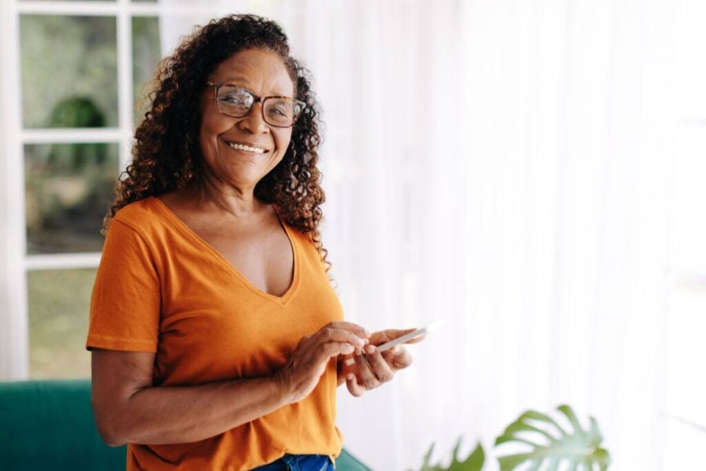 happy midlife woman with a phone in her hands smiles at the camera.