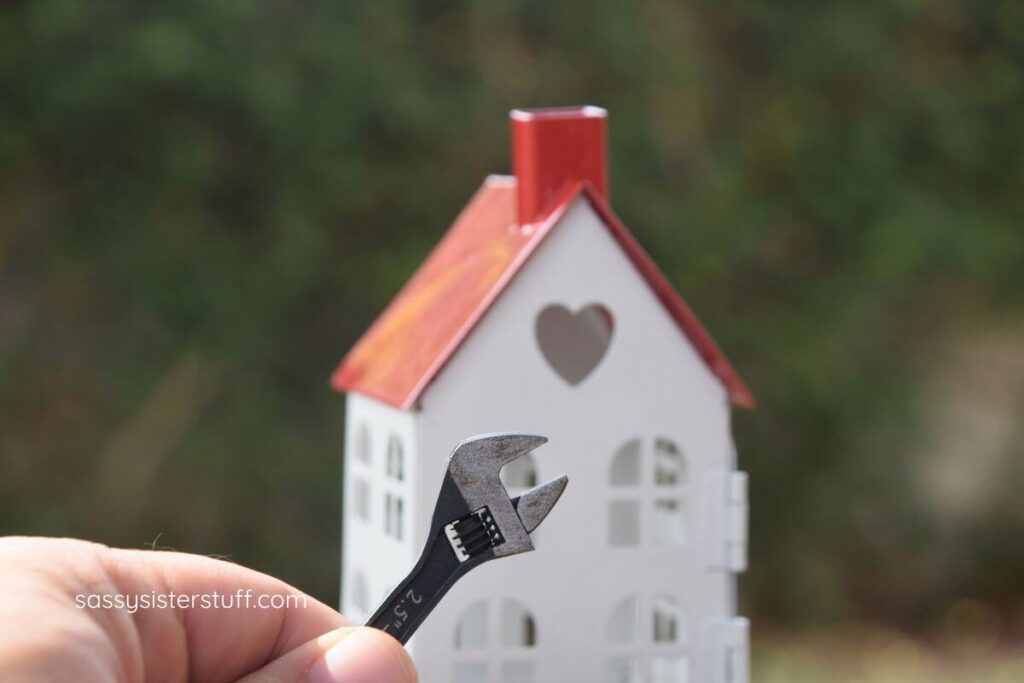 close up of a hand holding a wrench in front of a small white and red house.