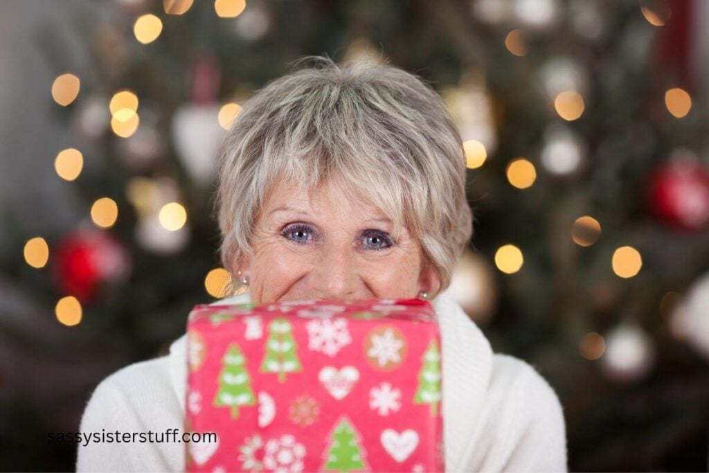 excited senior woman holds a wrapped gift in front of her lower face.