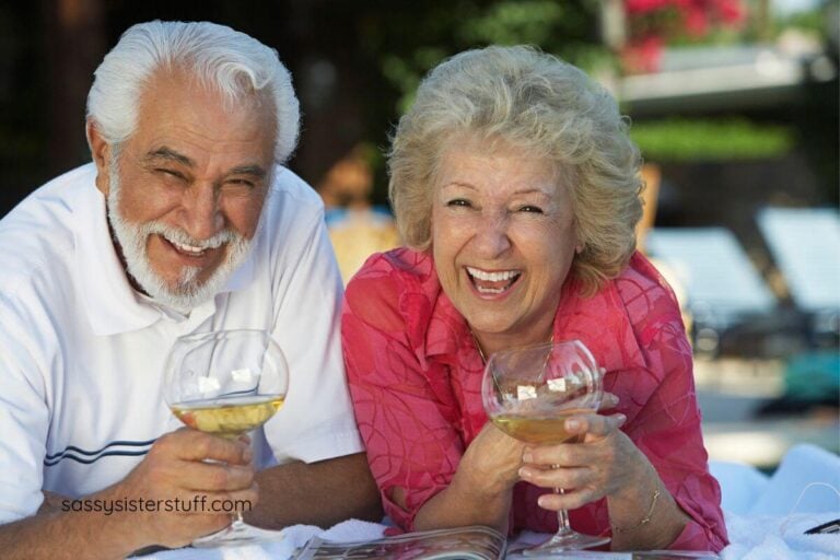 a middle aged couple lay on a blanket and enjoy a glass of wine together.
