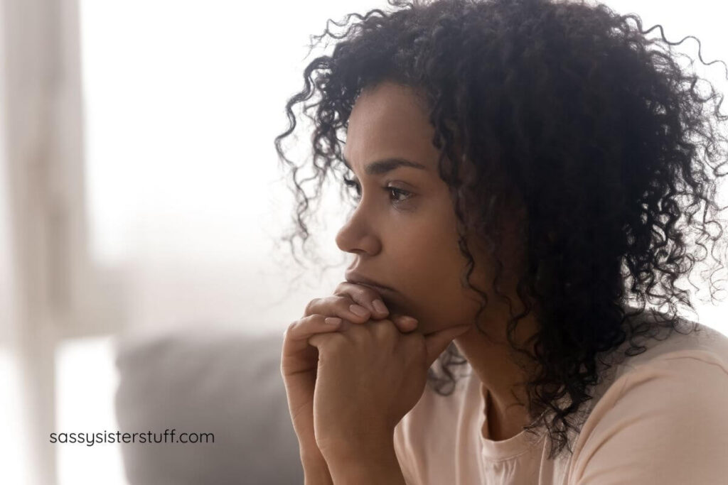 pretty African American woman sits with her hands clasped under her chin, pondering how to get out of her own way with her negative thoughts.