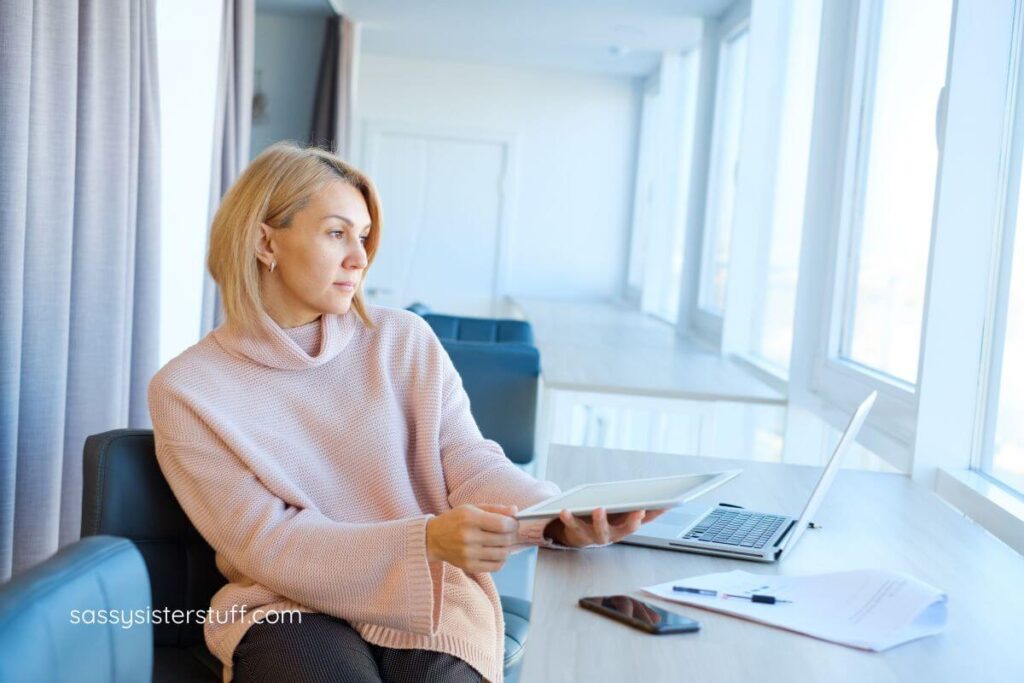 pretty woman absent-mindedly sitting with her notebook and laptop at her desk but not doing anything.