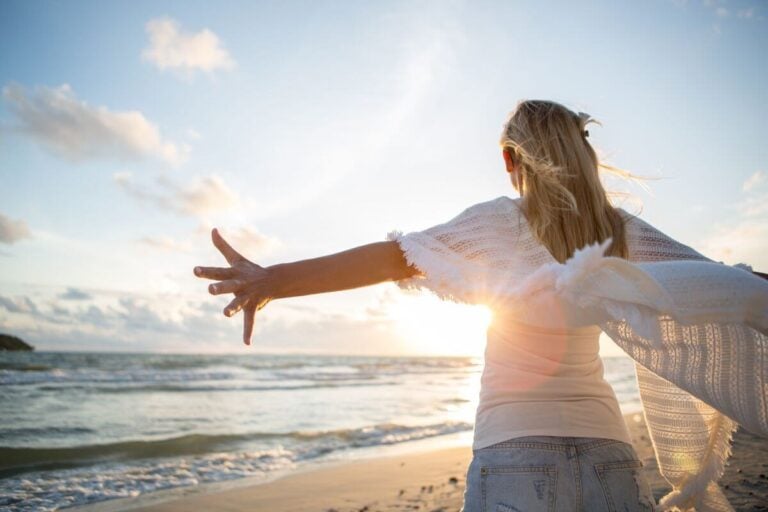 woman stands at the edge of the shoreline with her arms stretched out after reading some beautiful inspirational quotes.