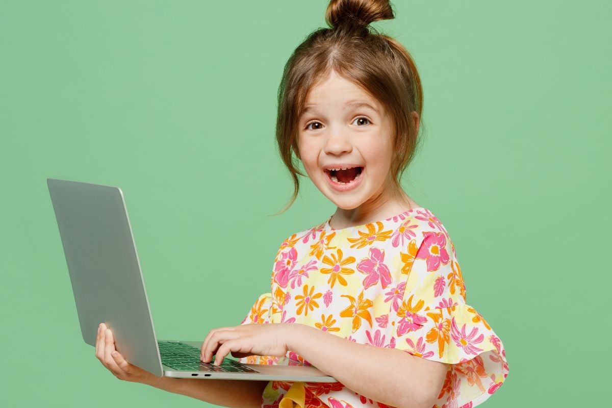 Little girl looking exited holding alaptop by green background