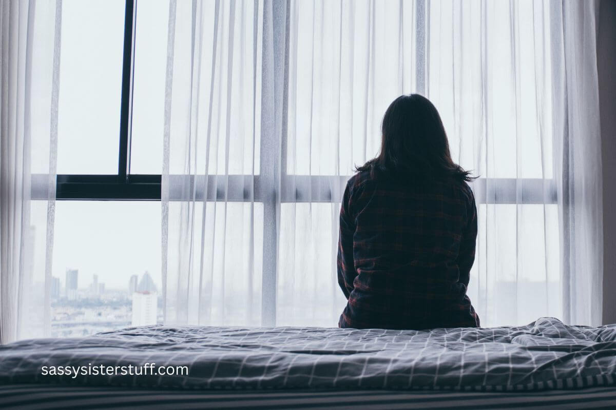 middle aged woman sitting on the edge of her bed feeling lonely.