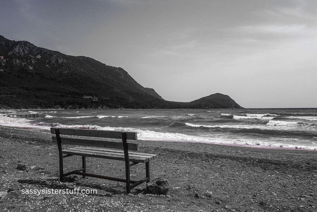 single bench on the beach at the edge of the ocean on a cloudy, dark day.