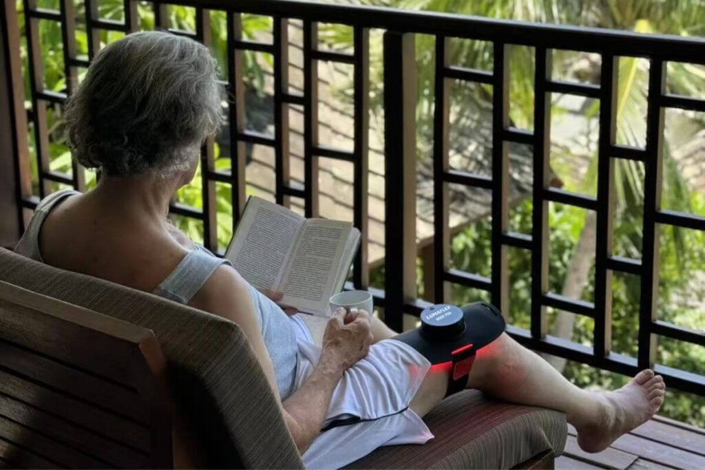 senior woman sitting on patio with red light therapy device on her knee.