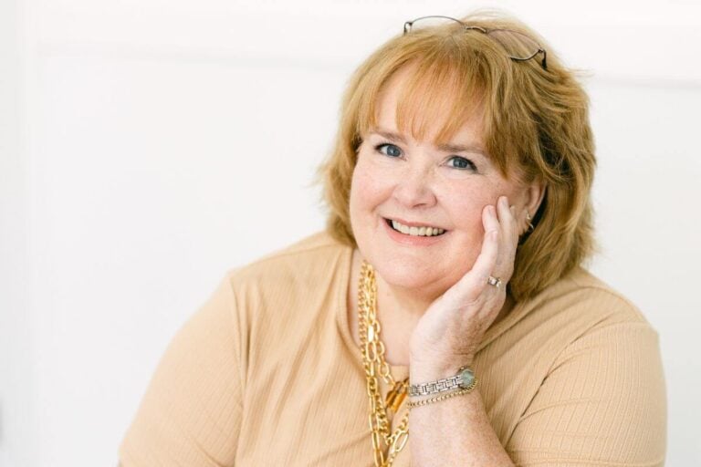 Founder of Sassy Sister Stuff models gold jewelry as she casually sits with her head resting on her hand.