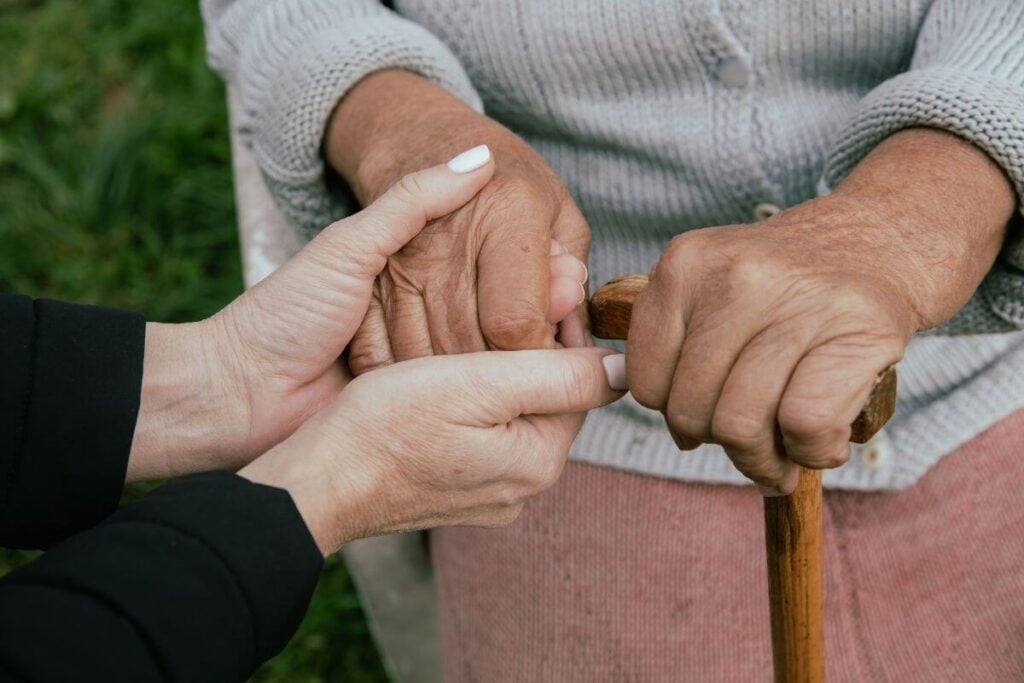a top view close-up of an adult daughter holding her elderly mother's hands.