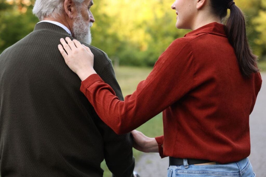 an adult daughter touches her father gently on the shoulder as they begin a walk down the trail.