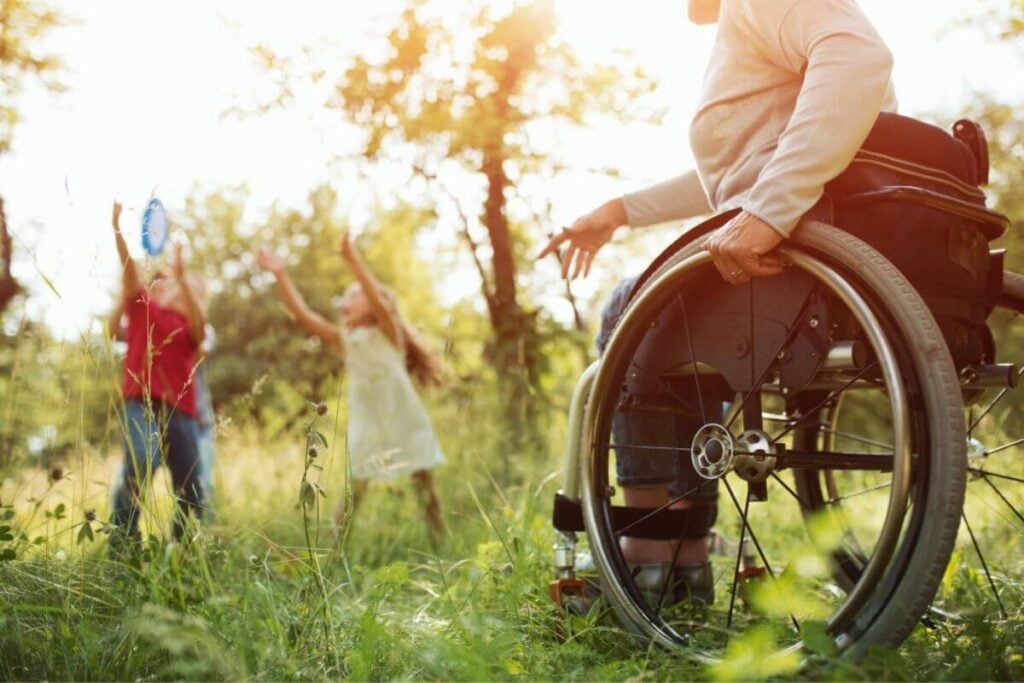 close-up of woman sitting in a wheelchair tossing a frisby across the yard to her grandchildren.