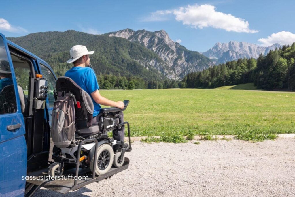 young man in an electric wheelchair gets out of an accessible van with mountains in the background.