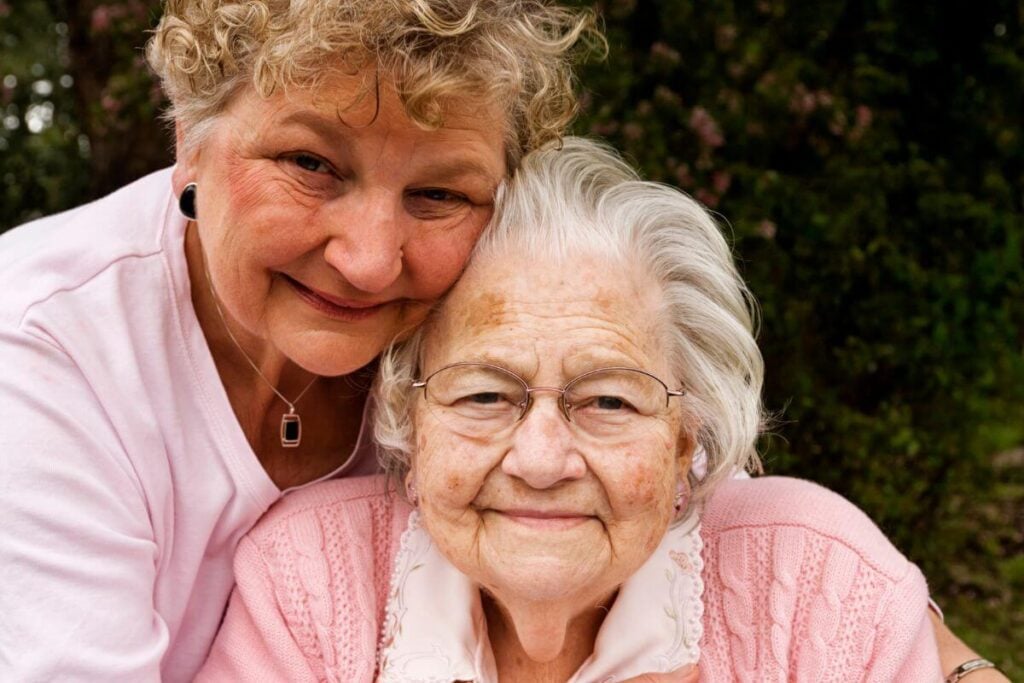 adult daughter hugs her elderly mother from behind.