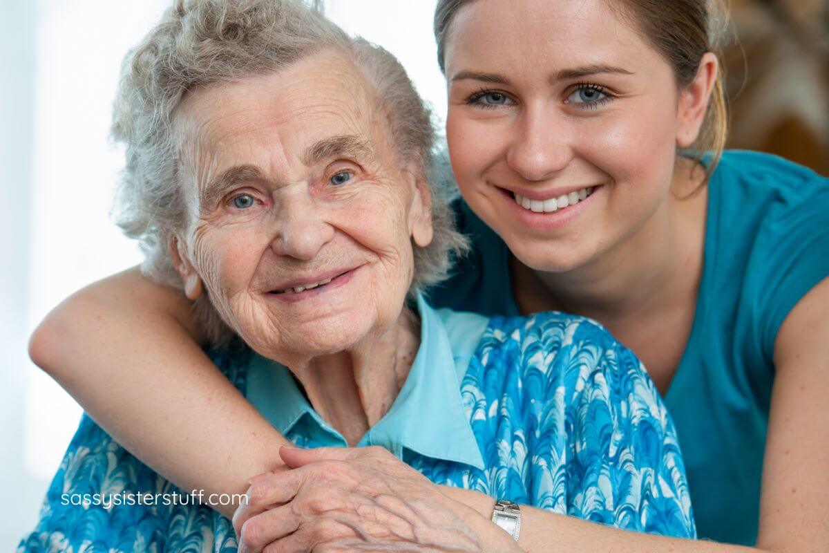 elderly mother and adult daughter smile for the camera.