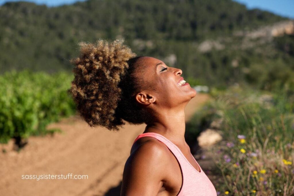 beautiful midlife African American woman smiles and looks up at the sun with her eyes close because she has finally figured out she doesn't need a purpose in life.