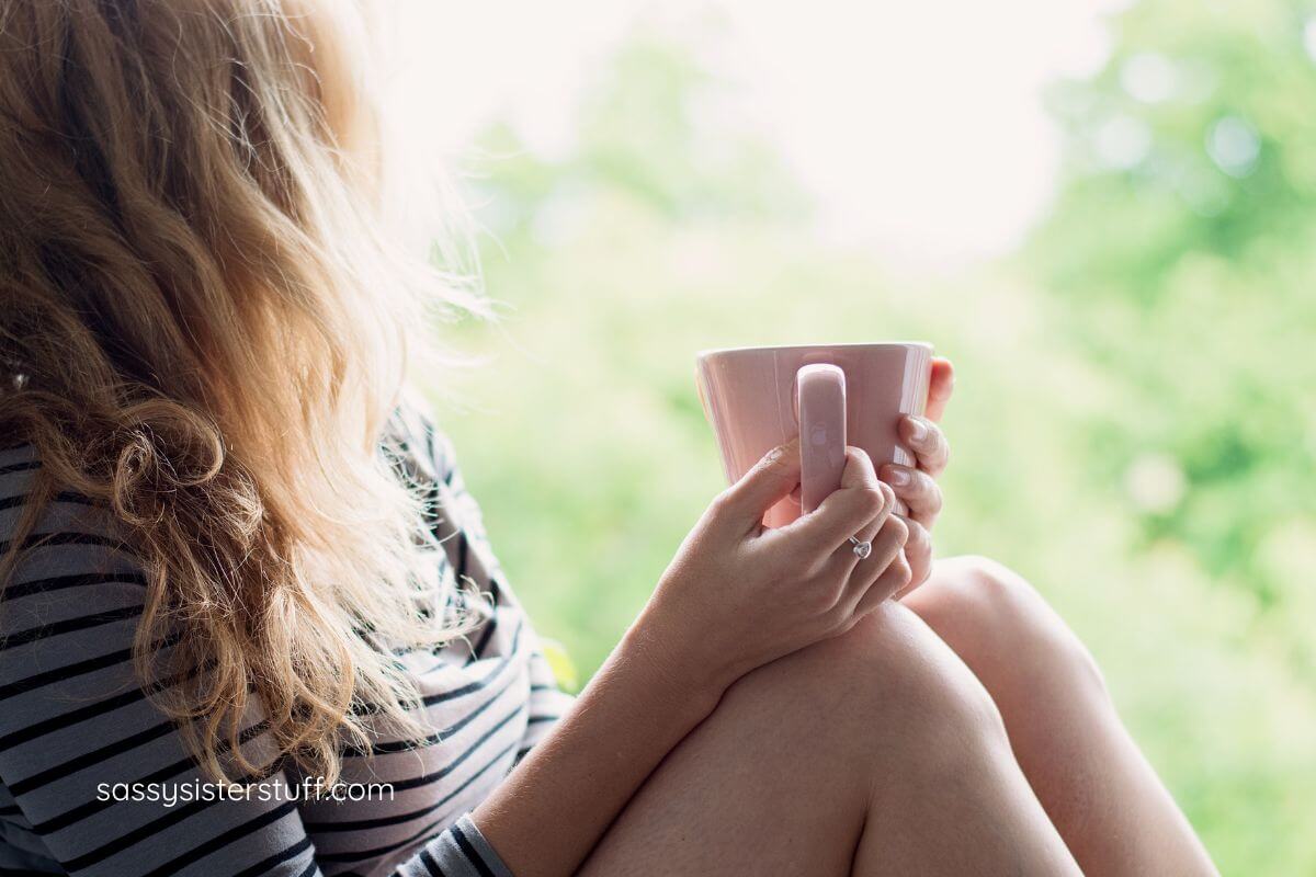woman with long blonde hair relaxes on a windowsil with a cup of tea because she finally feels the freedom of living without a purpose in life.