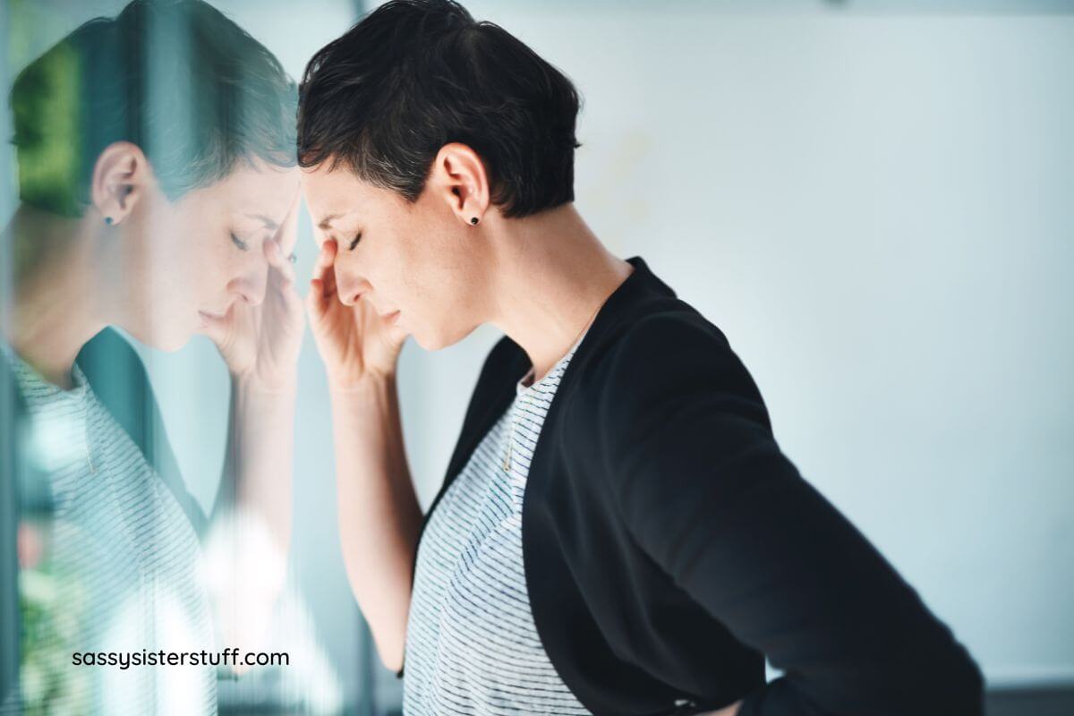 midlife woman with her forehead pressed against a window pine and her hand up to her face.