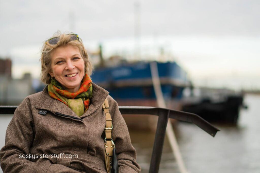 middle aged woman since on a pier and smiles while traveling.