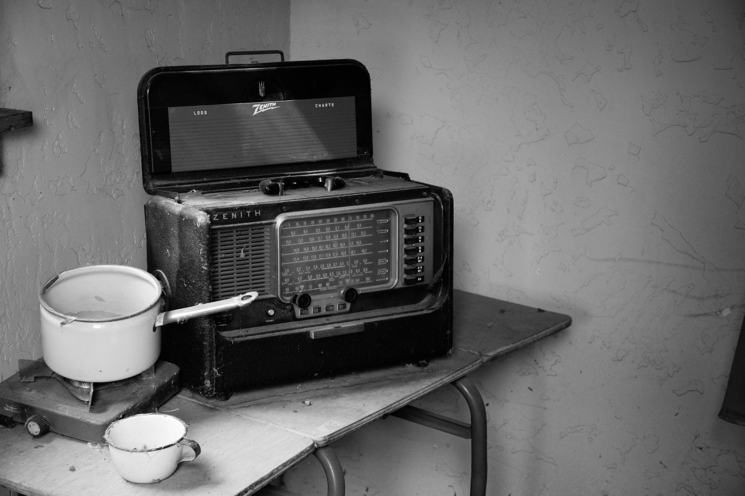 Black and white photo of an old Zenith radio with enamel pot and mug on a rustic table.