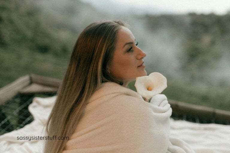 middle aged woman wrapped in a blanket peacefully sitting outside in nature to get grounded.